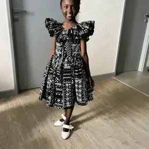High-quality Kitenge black and white patterned dress with durable ruffled sleeves and flared skirt; every purchase supports Africa.