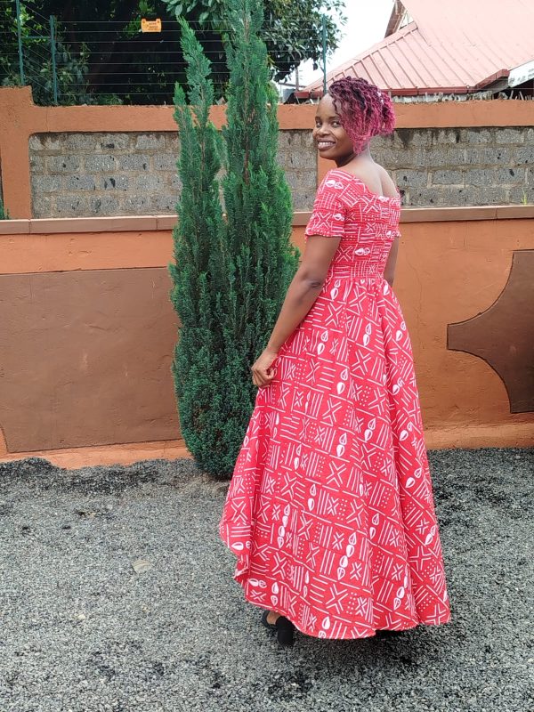 Customizable Kitenge dress with red and white patterns, high-low hemline, and durable fabric. Supports communities in Africa.