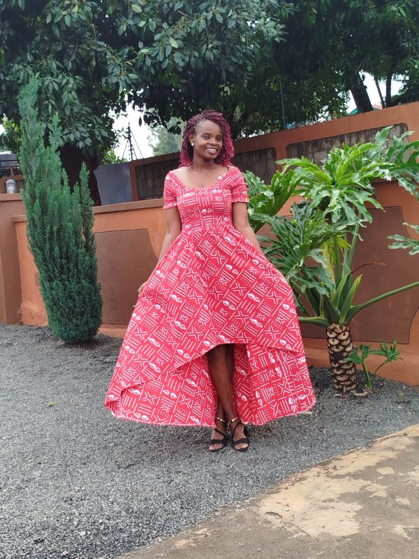 Customizable Kitenge dress with red and white patterns, high-low hemline, and durable fabric. Supports communities in Africa.