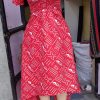 Customizable Kitenge dress with red and white patterns, high-low hemline, and durable fabric. Supports communities in Africa.