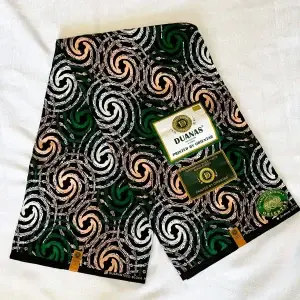 Premium Cotton Kitenge fabric featuring bold swirling patterns in green, white, and beige on a striking black backdrop, crafted from durable African cotton.
